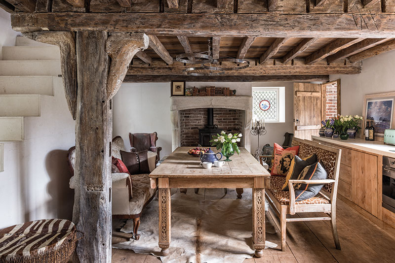 A Charnwood stove is set into an 18th-century French limestone fire surround, giving the kitchen a warm glow on winter evenings. McNeill designed the solid oak cabinetry which harmonises with the heavily beamed ceiling and the wide timber floorboards. Hanging above the dining table are circular stainless-steel ceiling lights inset with LEDs designed by McNeill. The landscape painting propped on the work surface is by Norfolk artist Jeremy Barlow