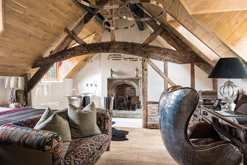 A partition wall between the bedroom and bathroom was built beneath a reclaimed cruck beam. The vintage chesterfield was reupholstered in a kilim rug bought at auction. The copper bath with tin finish is from William Holland