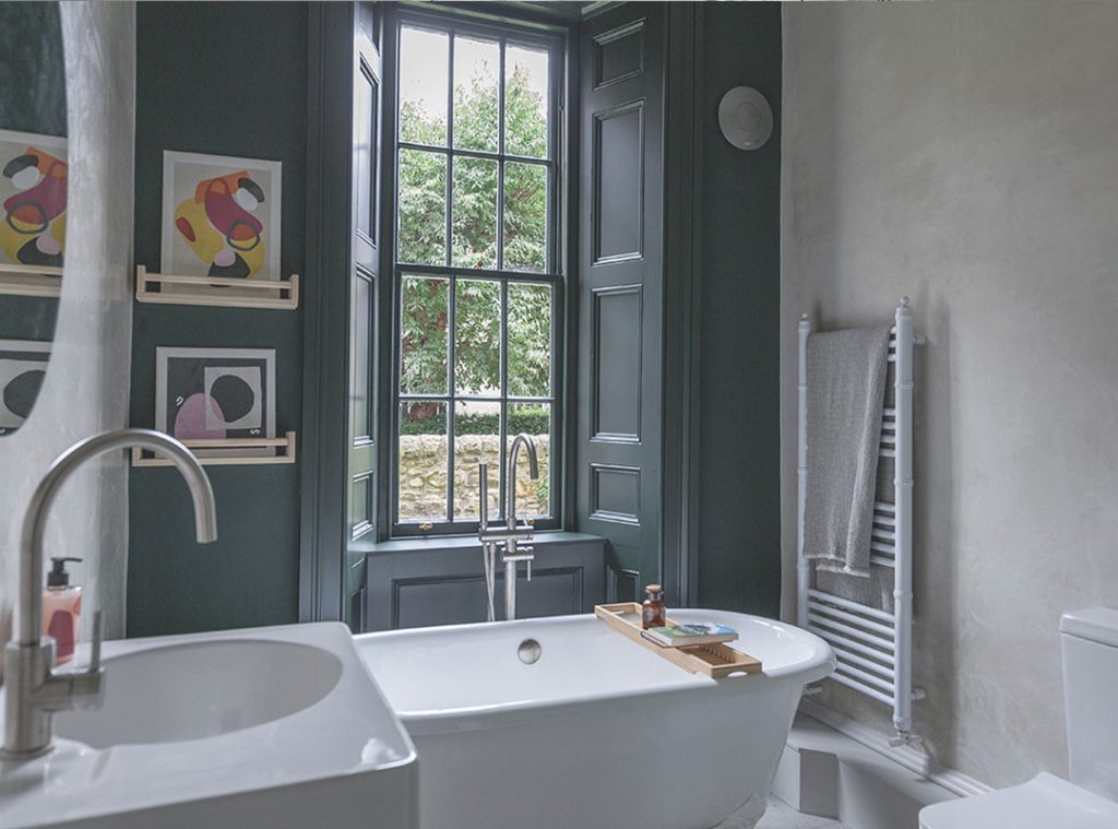 Bathroom with traditional shutters, an accent wall of dark paint, a large bath and abstract art. Stockbridge Edinburgh staycation