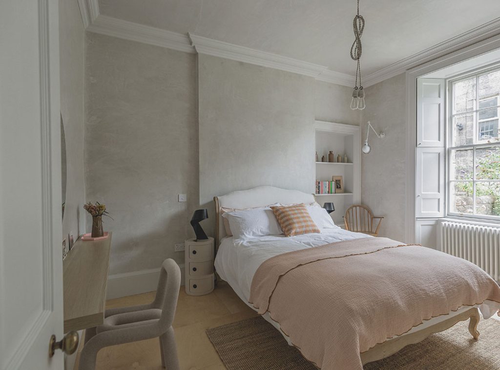 A neutral bedroom with a double bed dressed in white bedding and pale pink linen. The walls are finished with a plaster effect. Stockbridge Edinburgh staycation
