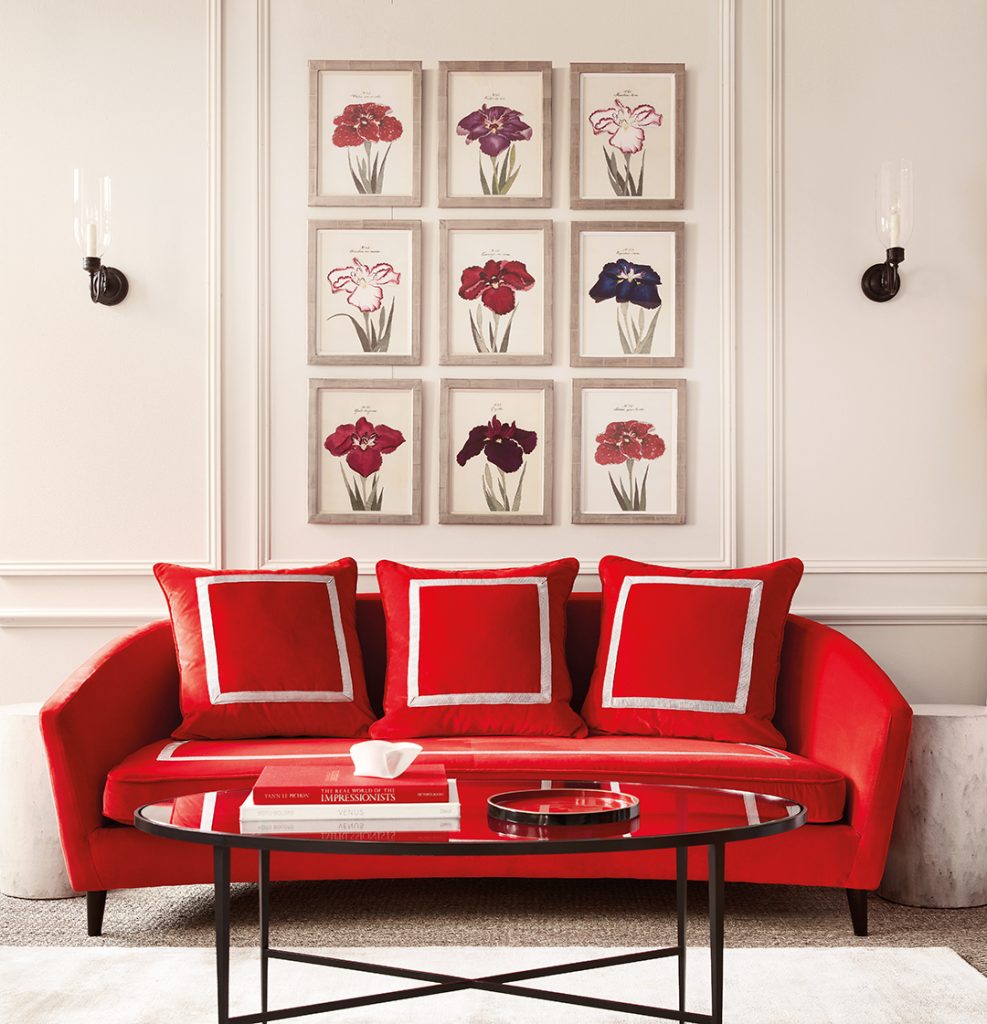 A bright red sofa with three scatter back cushions. Nine images of red, white, pink, and blue flowers are mounted on the wall behind.