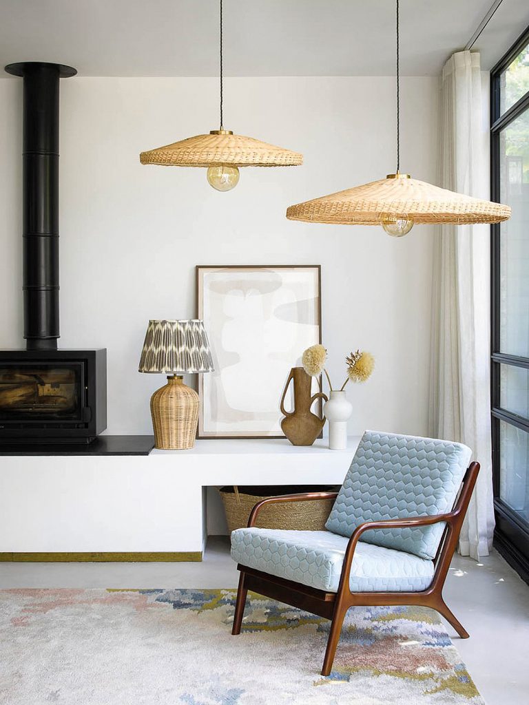 Two rattan pendants hang over a mid-century modern armchair. In the background, a woodburning stove sits atop a low built-in section