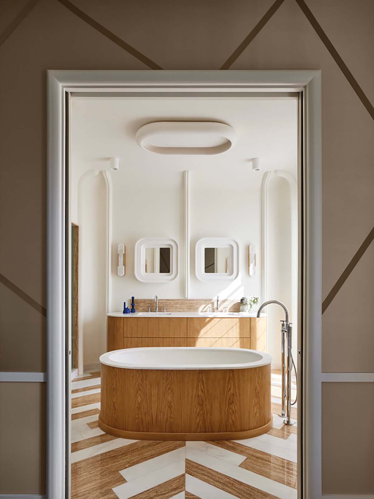 A bathroom in Paris, designed by Fabrice Jean featuring oak and plaster accents and a chevron patterned floor made up of travertine and white Macael marble