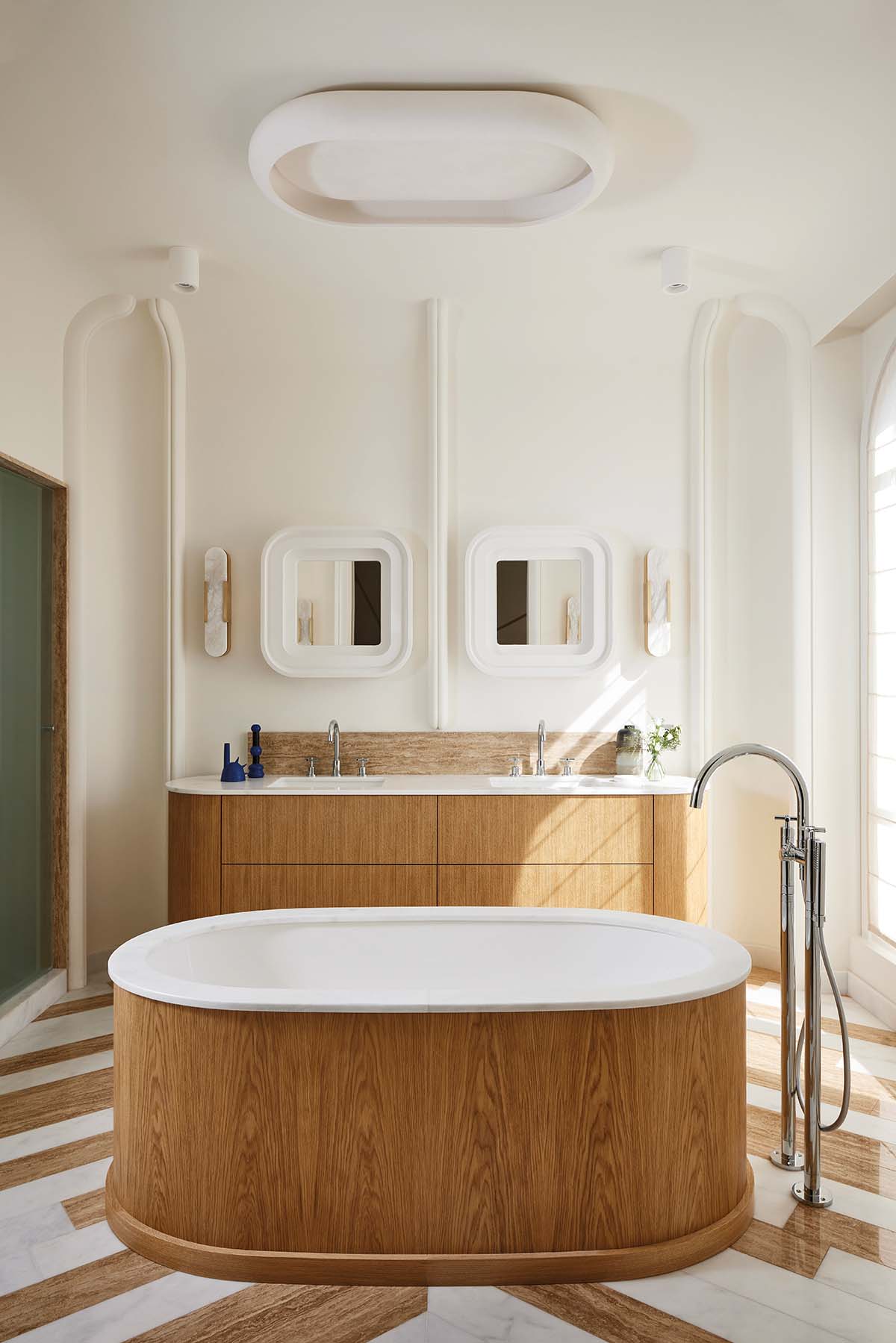 A bathroom in Paris, designed by Fabrice Jean featuring oak and plaster accents and a chevron patterned floor made up of travertine and white Macael marble