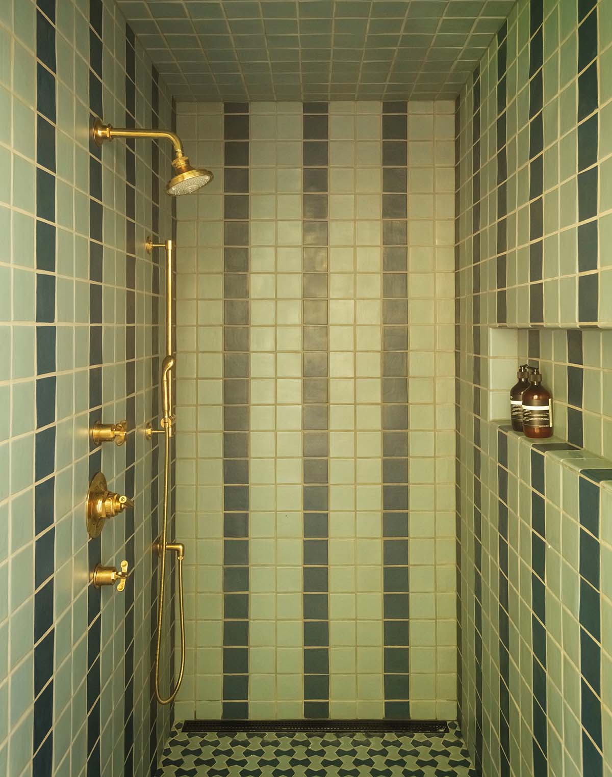 A shower tiled in two shades of green, creating a pattern of vertical stripes. Shower fittings are in gold.