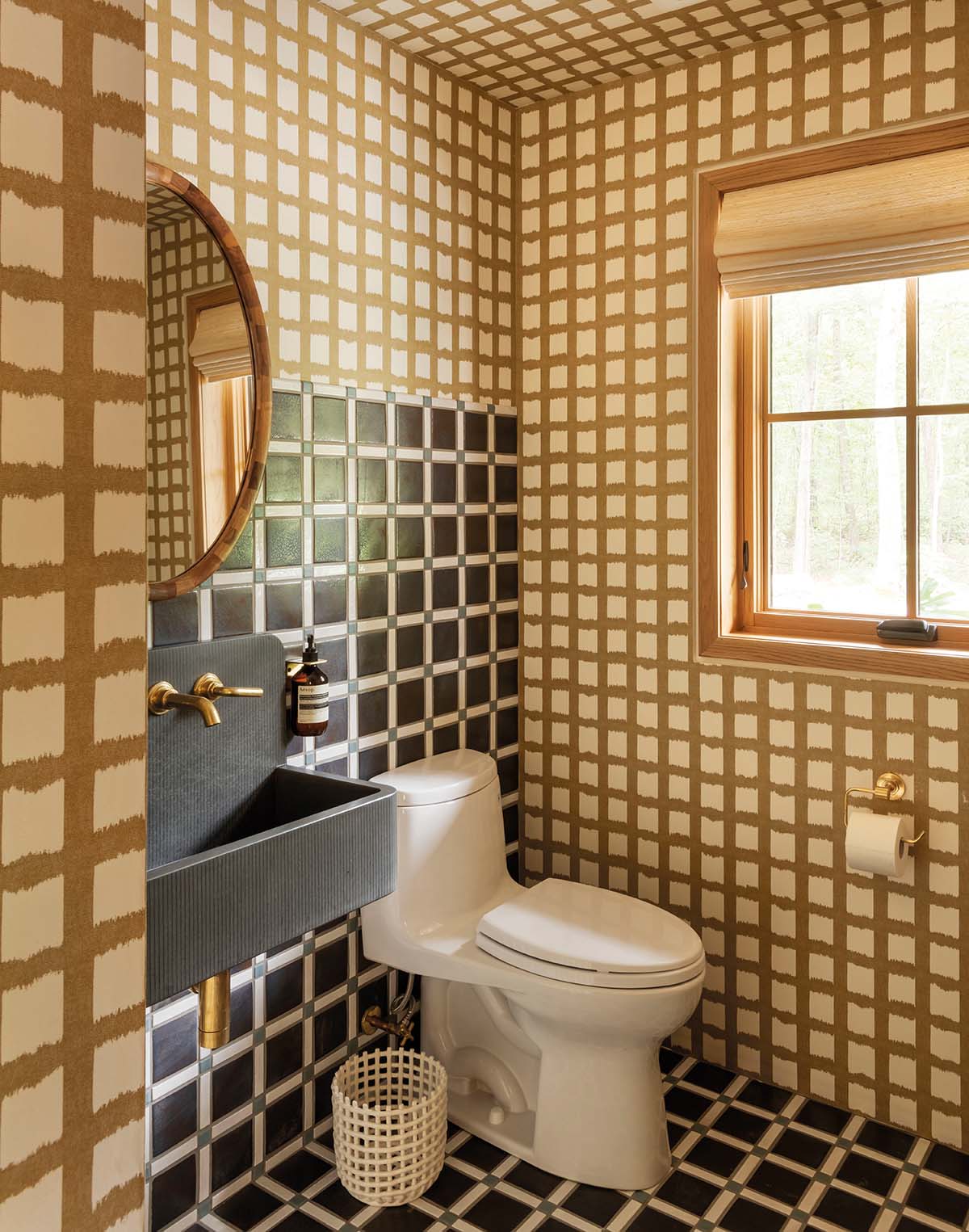 A bathroom. The sink is black with gold taps and the walls are patterned in two types of check, one brown and white and the other white, charcoal and green and covers the floor and area behind the sink and toilet.