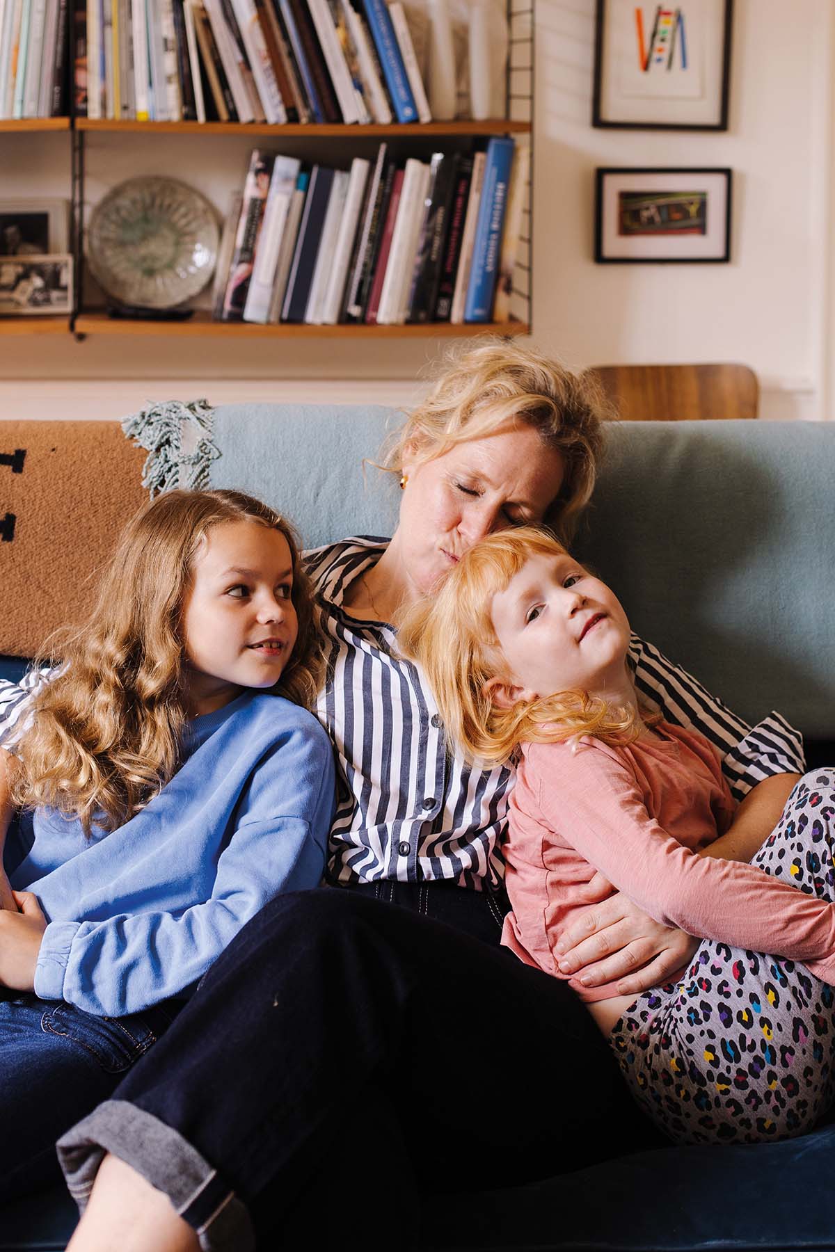 a mother cuddles two daughters on a sofa