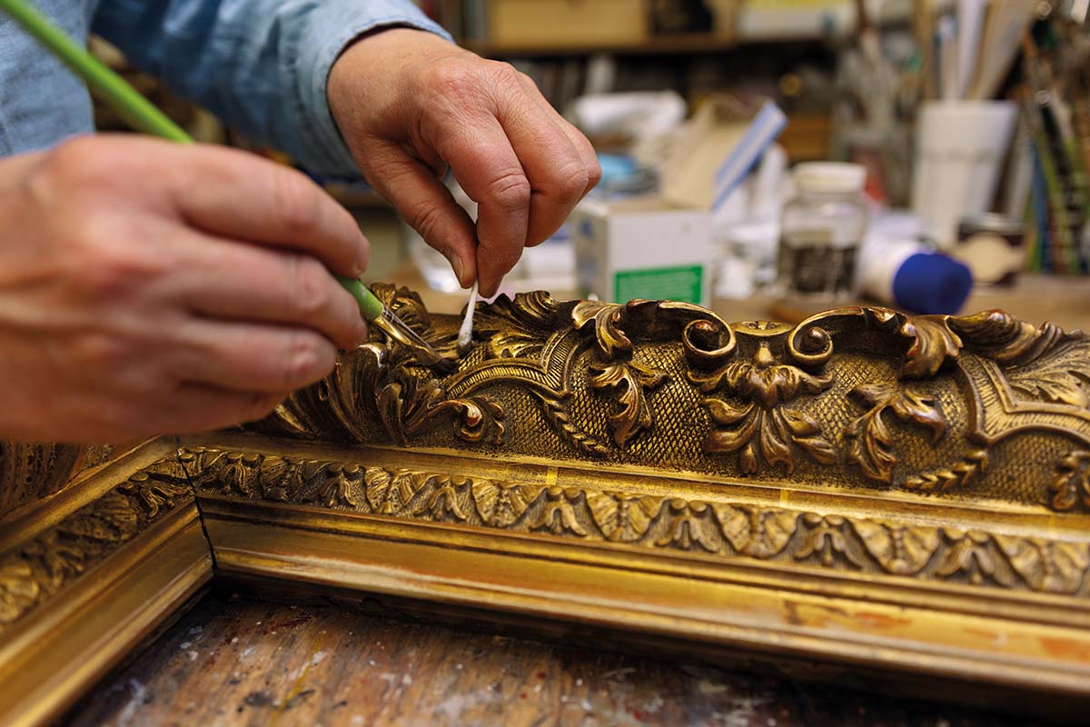 A conservator works on the gilding of a picture frame