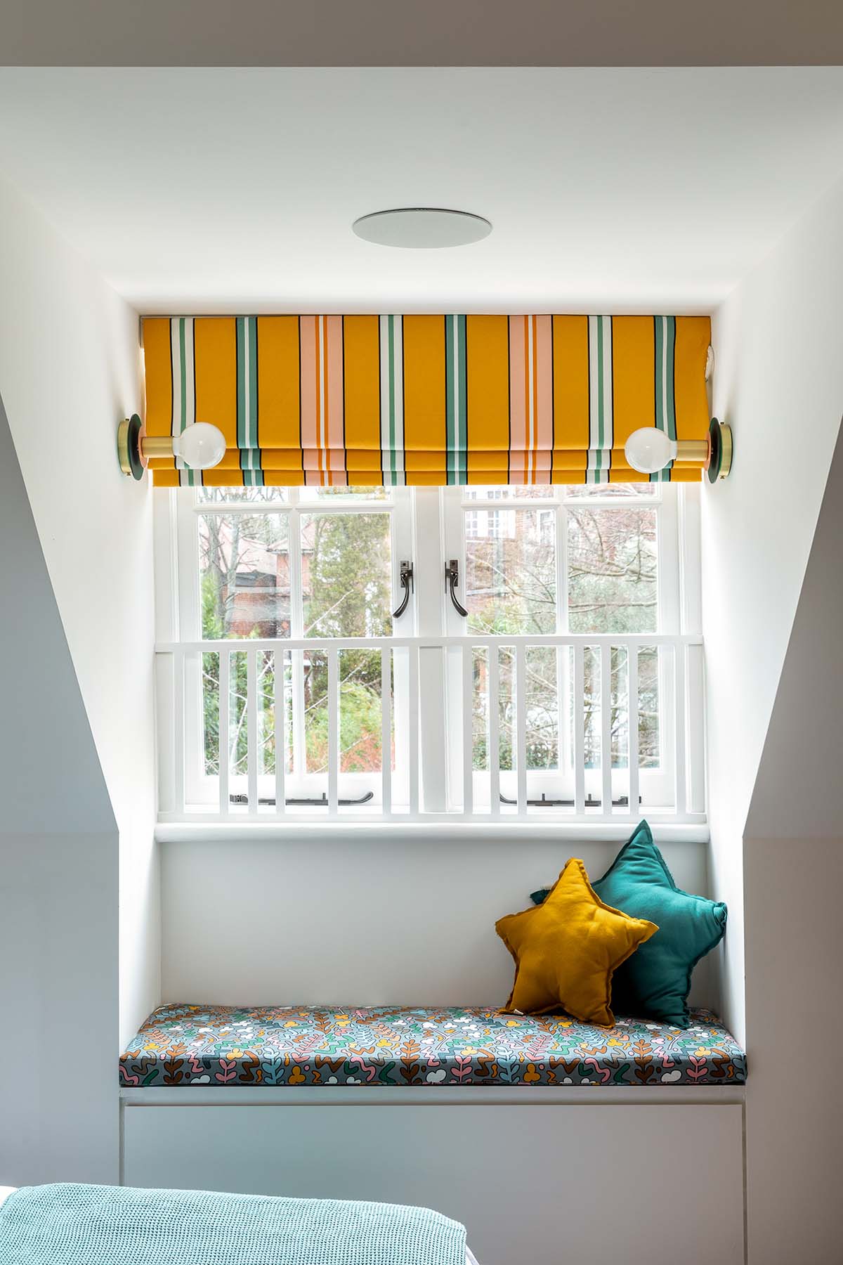 A children's room with a stripy roman blind and star cushions, designed by Mia Karlsson