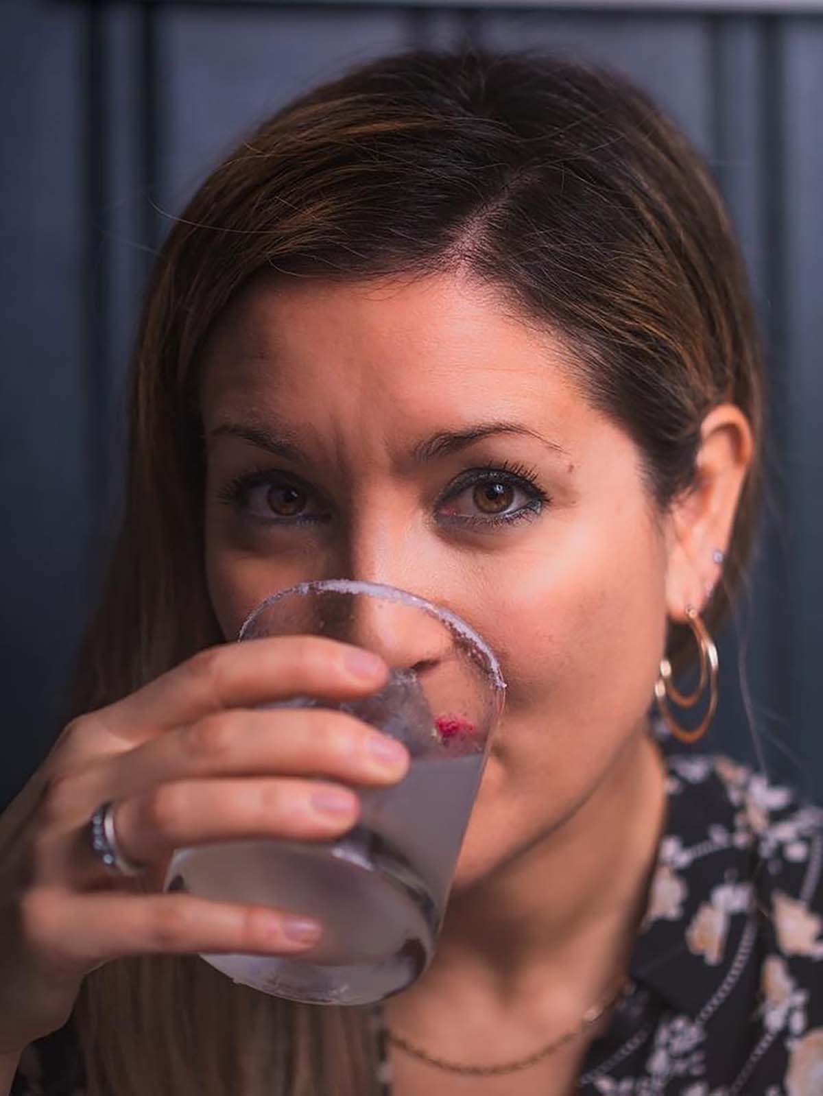 a woman sips a cocktail and looks at the camera