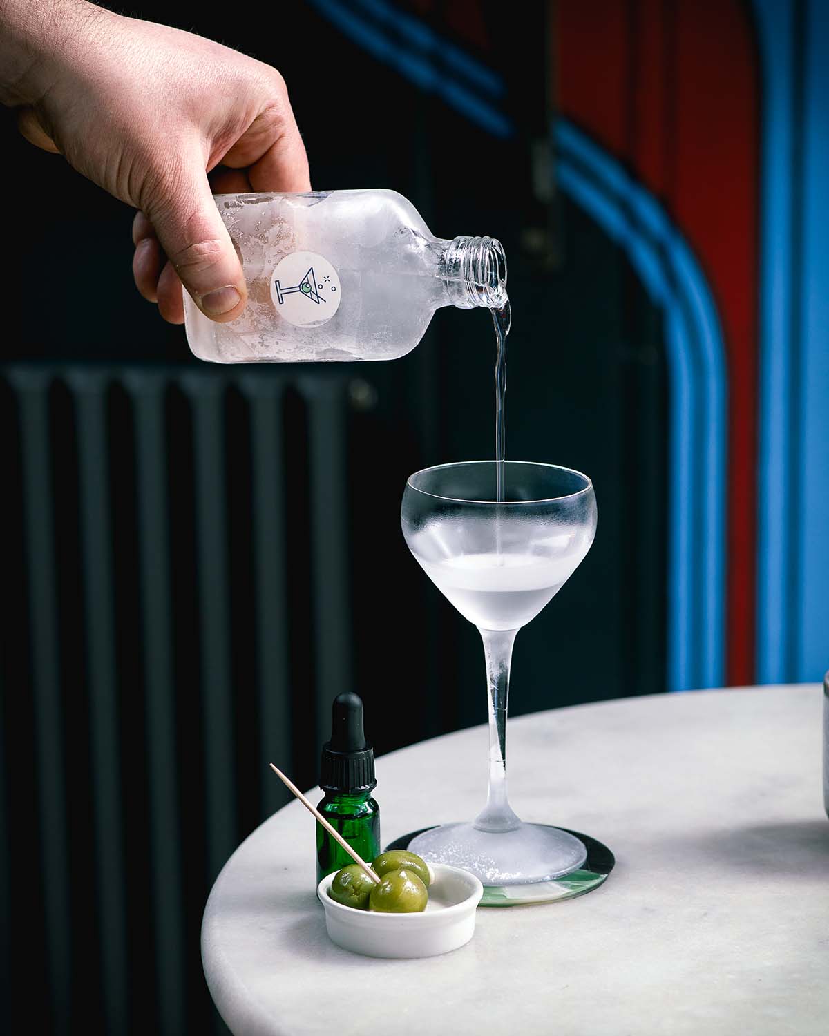 a hand pours a frozen martini from a small bottle into a chilled glass