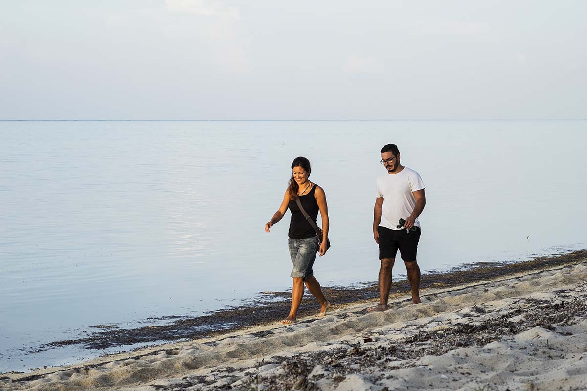 A man and a woman walk on a sandy beach