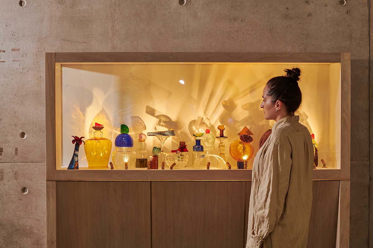 A woman stands in front of a display cabinet filled with glass pieces
