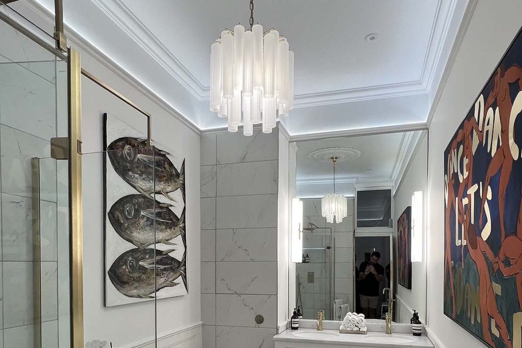 a bathroom with white tiling, gold accents, a painting of fish and a painting of dancing figures