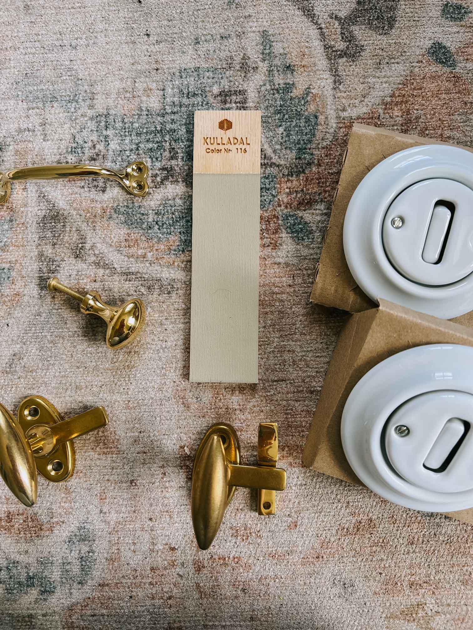 a close up of kitchen details, including brass handles, a colour swatch of the cabinetry and light switches