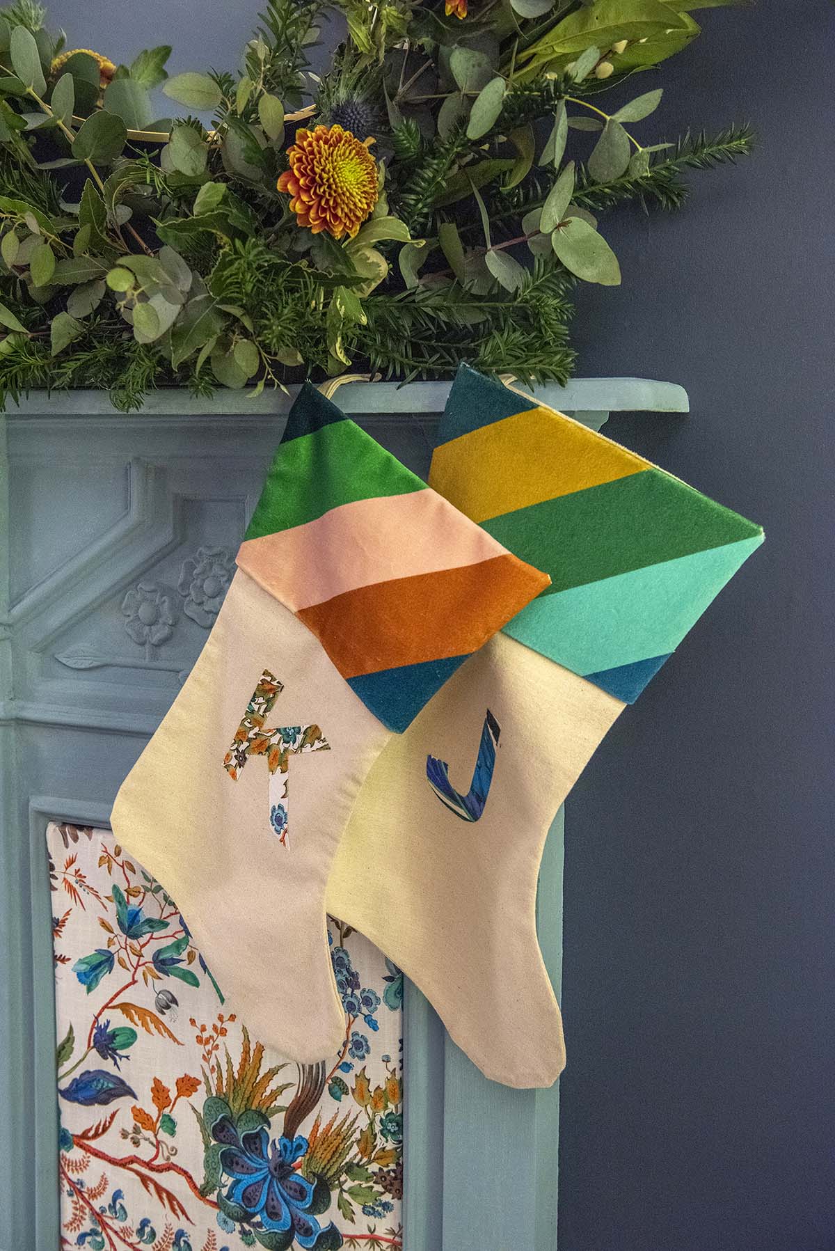 Two stockings hang on a mantlepiece, embroidered with the letters K and J