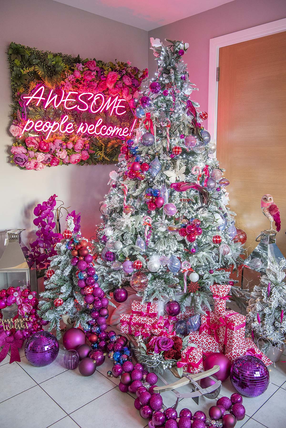 A Christmas tree decorated with pink and silver, standing in front of a pink neon light