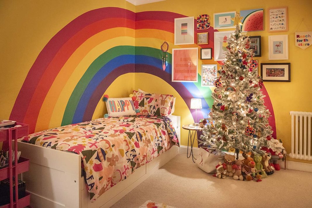 a children's bedroom with a rainbow on the wall and a colourful Christmas tree