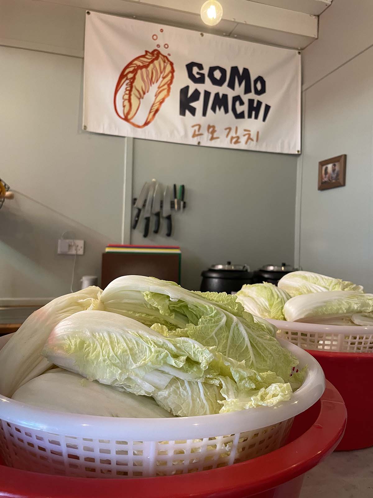 two large baskets of Korean cabbage sit under a sign saying 'Gomo Kimchi'