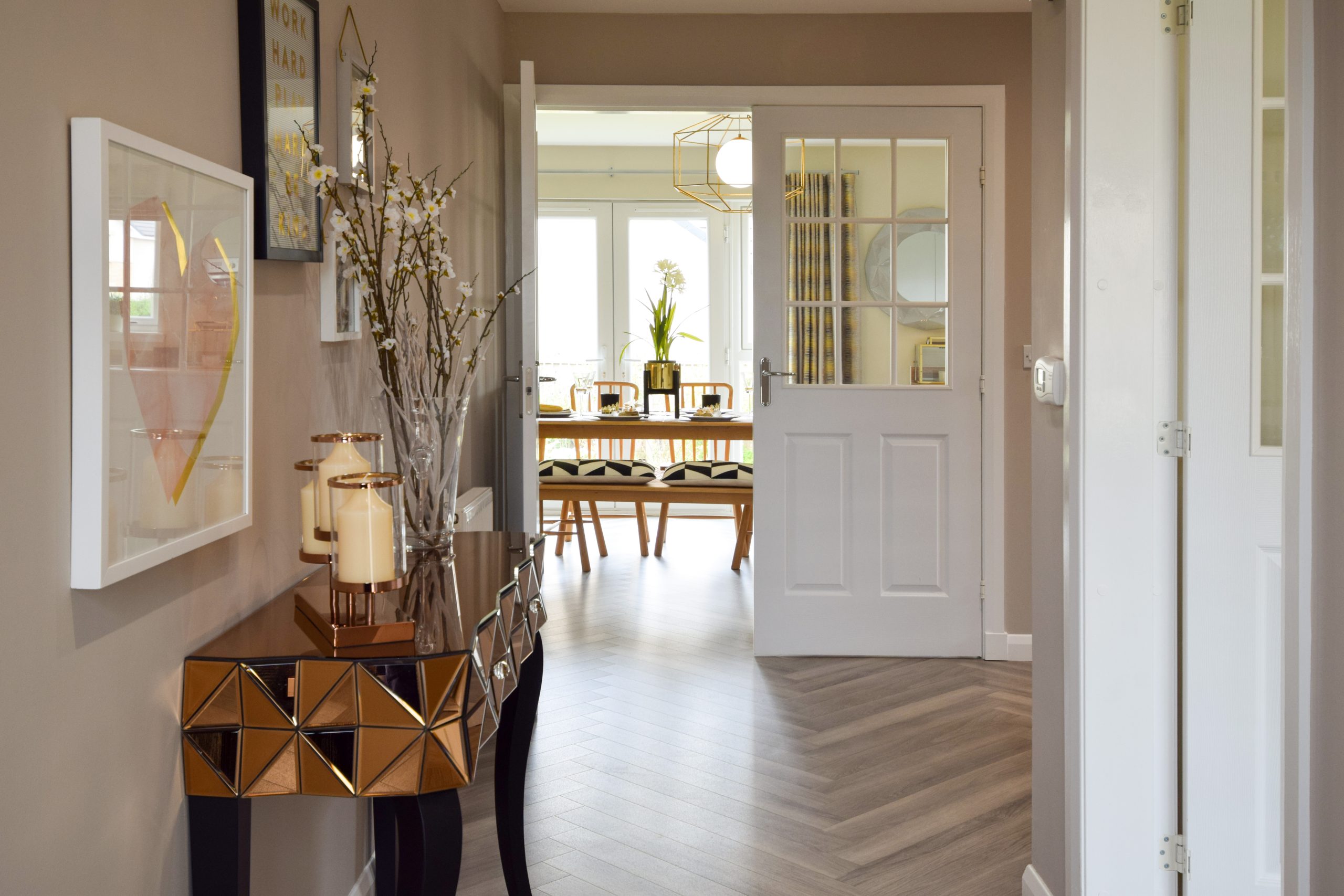 an entrance hall with table, chevron floors and double doors which open onto a dining room