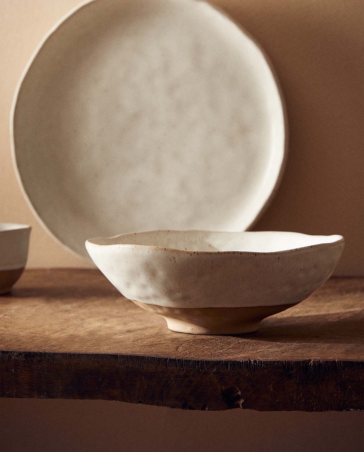 A textured ceramic stoneware bowl on a wooden countertop, with a matching plate behind it
