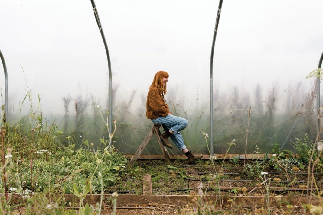 Fiona Inglis sitting on a stepladder inside one of the polytunnels, amongst rows of planting