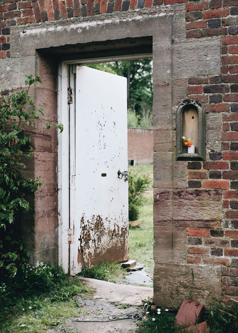 The narrow entrance to the. walled garden. An unassuming white door set within a red brick wall