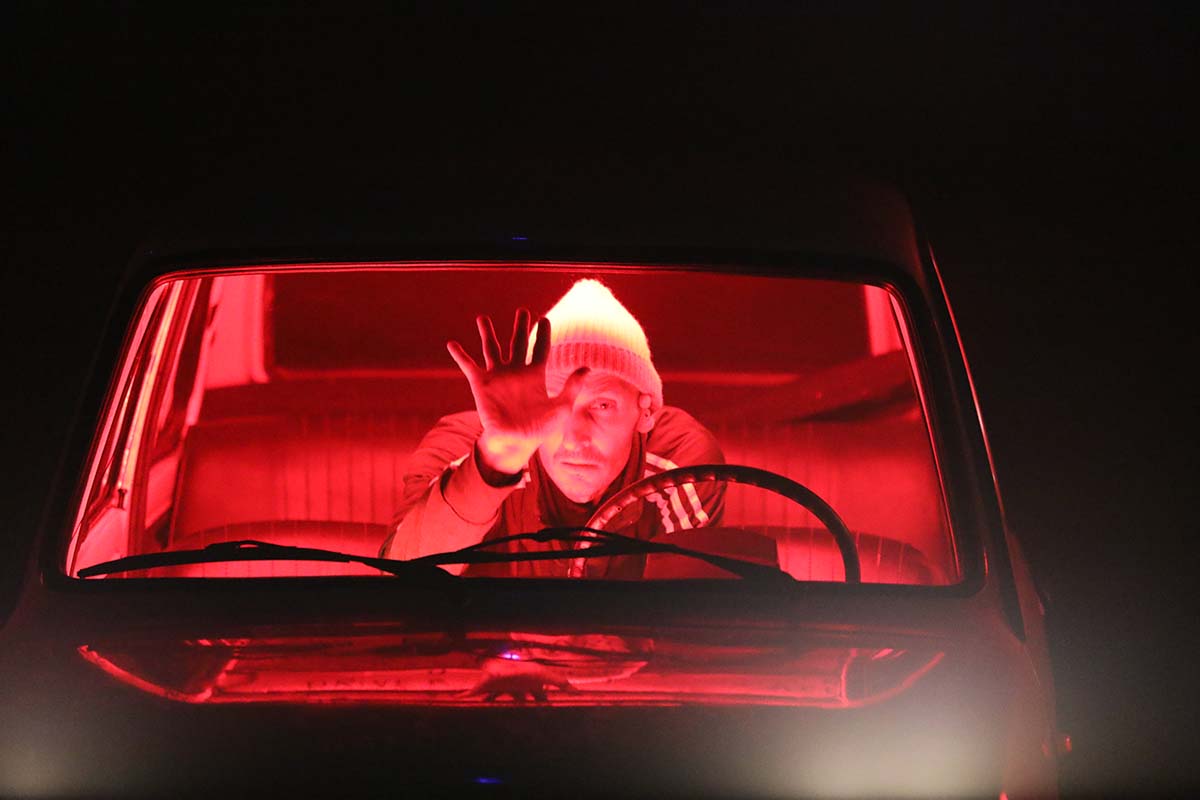 a man looks through a car windscreen. the interior of the car is lit by a red light