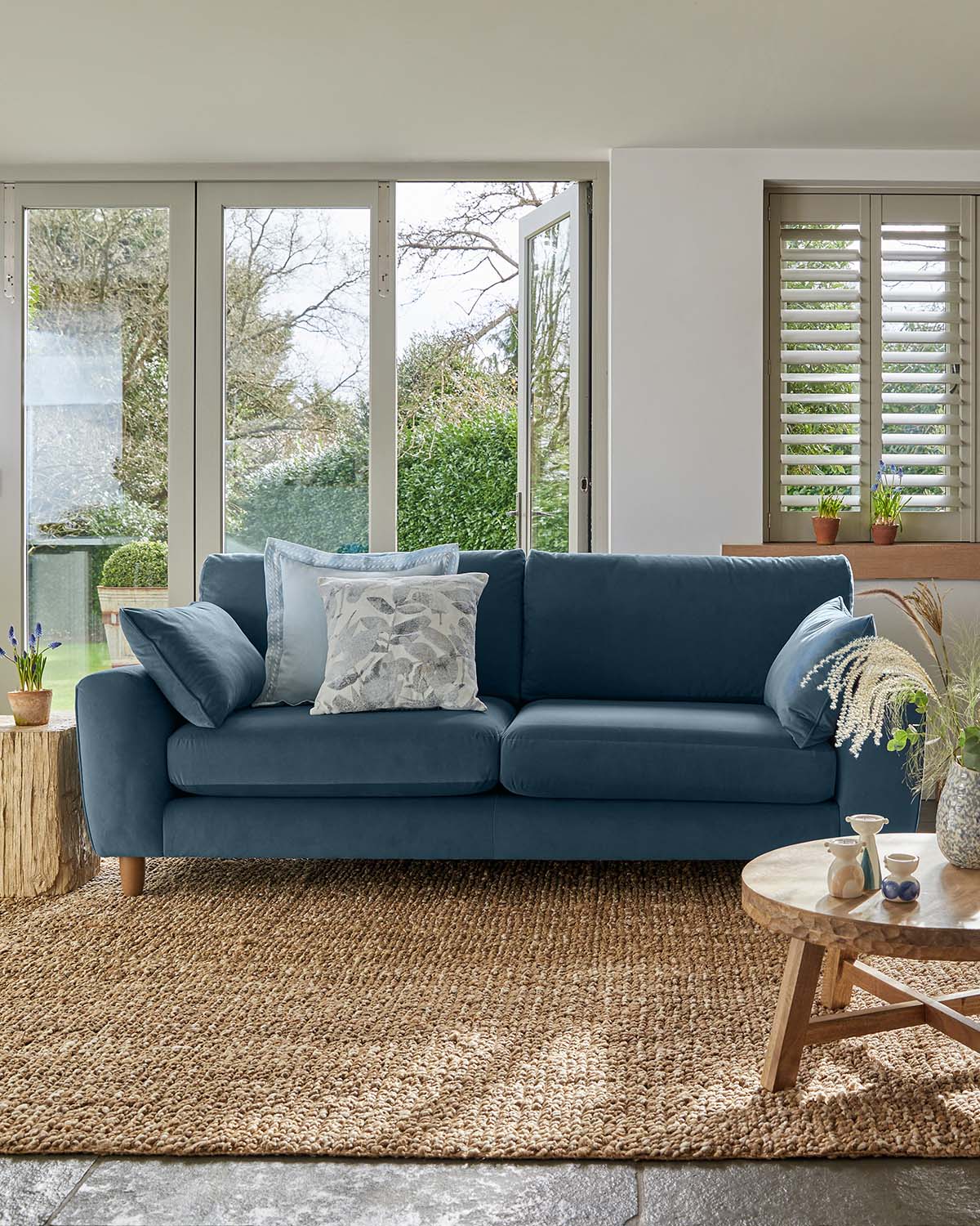 Blue sofa sitting on natural jute rug with windows behind it