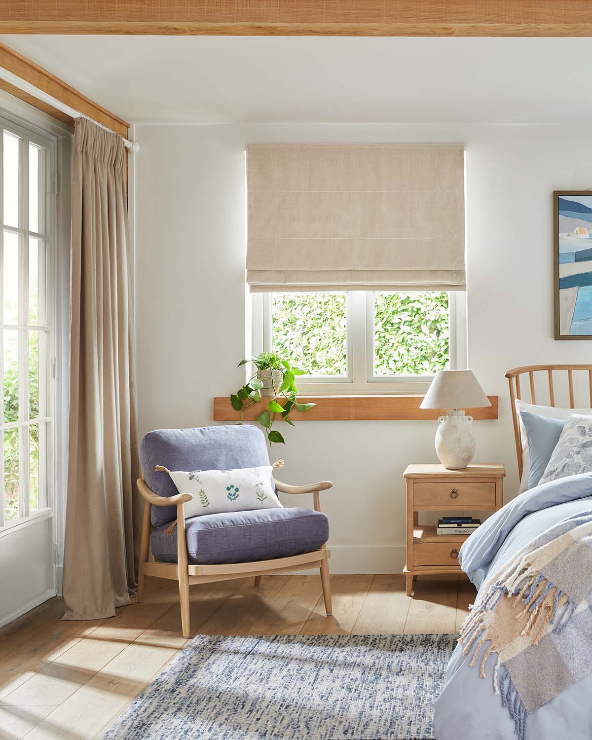 wooden chair in corner of light and bright bedroom with part of bed visible and blue rug