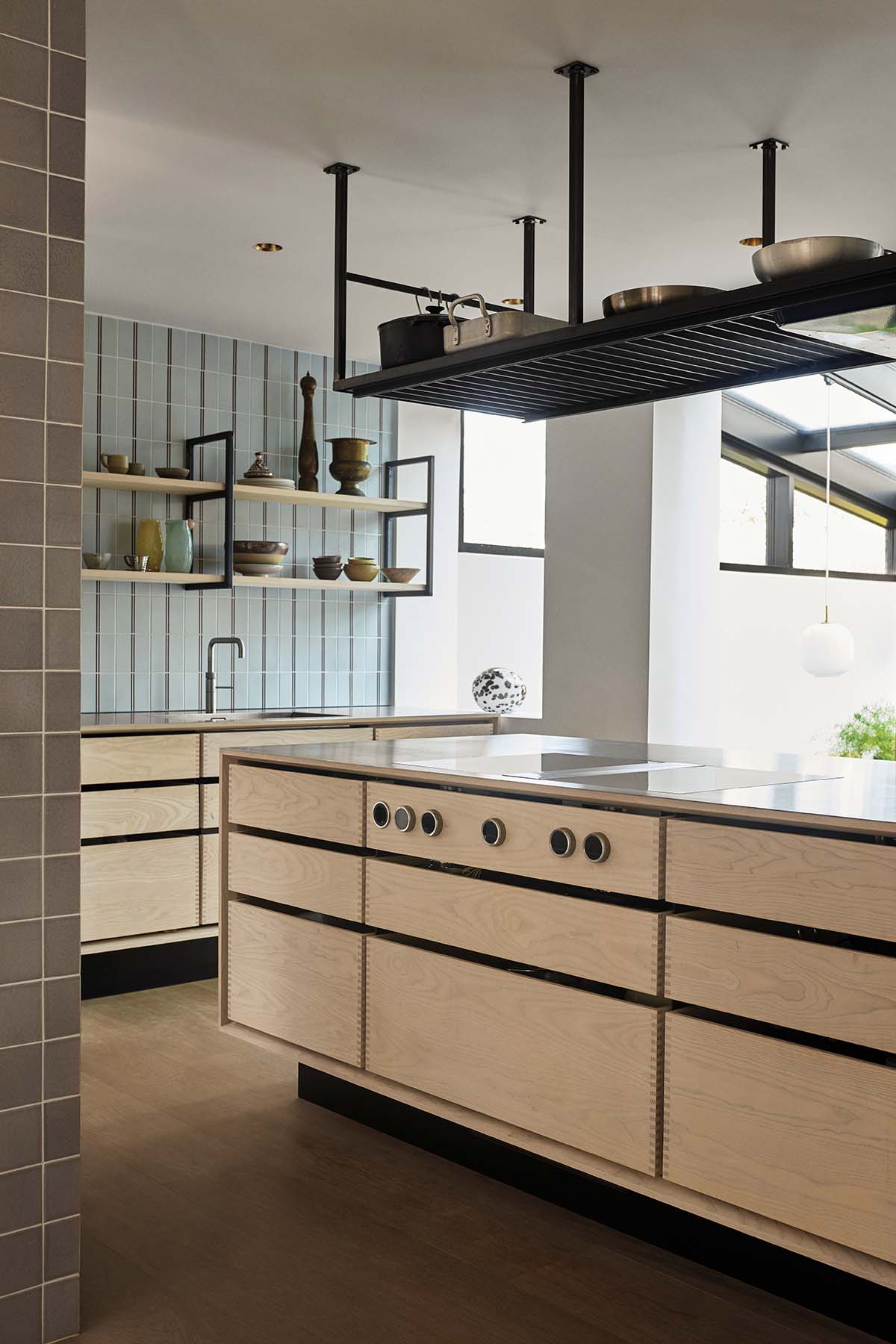 Kitchen island and food prep area, with wood drawers, white cabinetry and iron ceiling shelving featured in a bespoke design