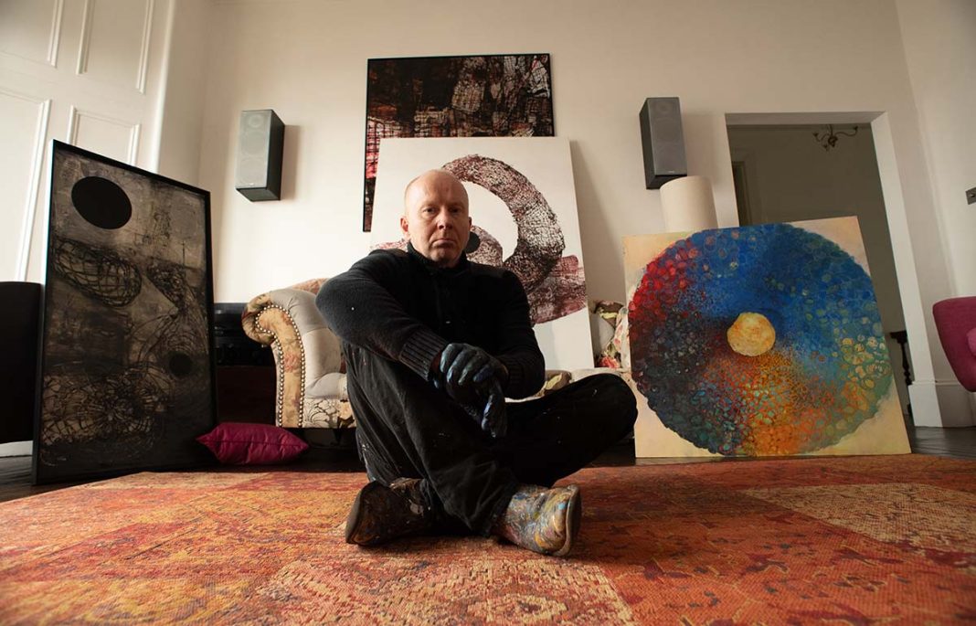 Gregor Harvie at home in Glasgow with paintings from recent physics-inspired work