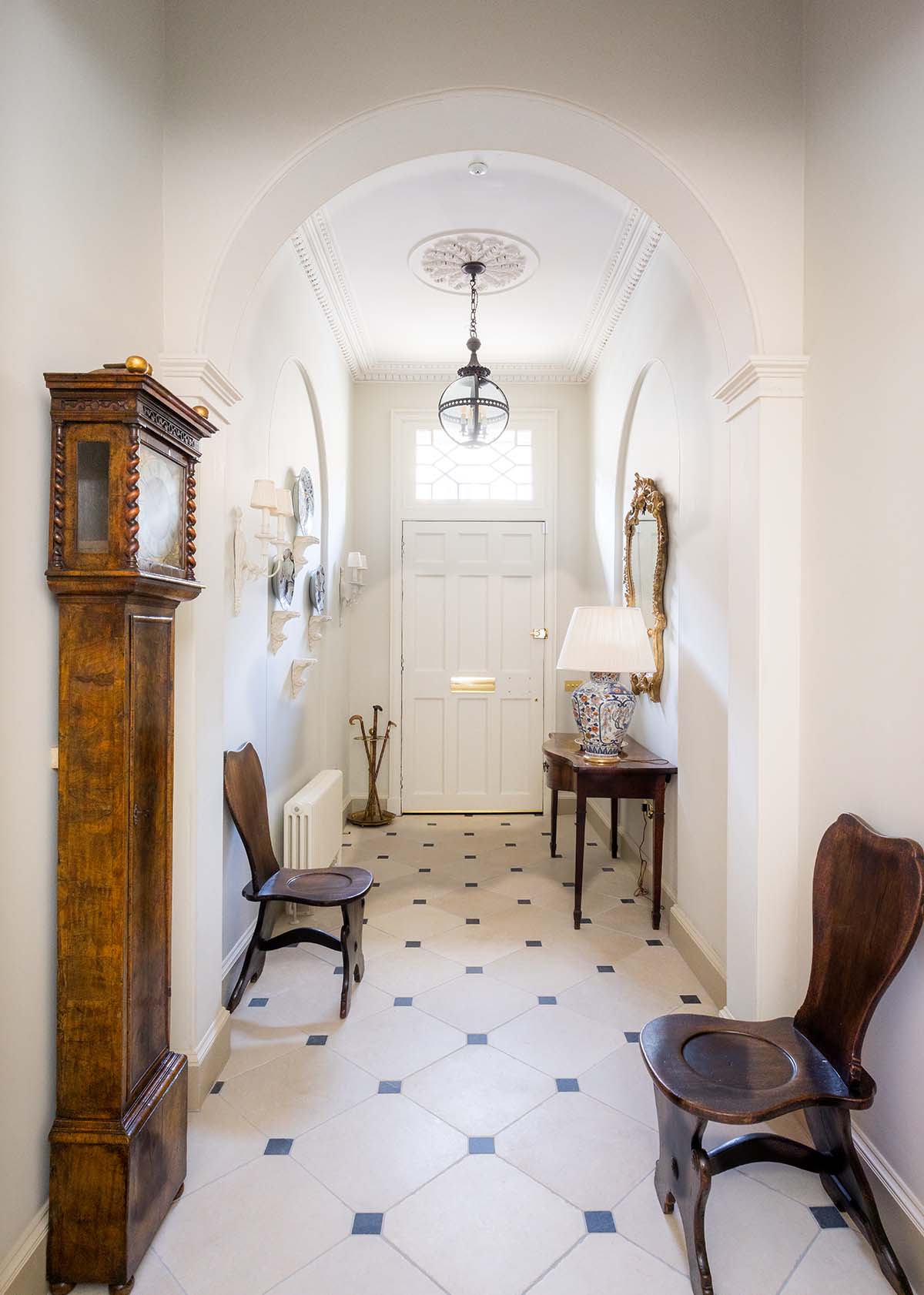 hallway of edinburgh townhouse with white walls, tiled flooring and antique chairs, mirrors and grandfather clock