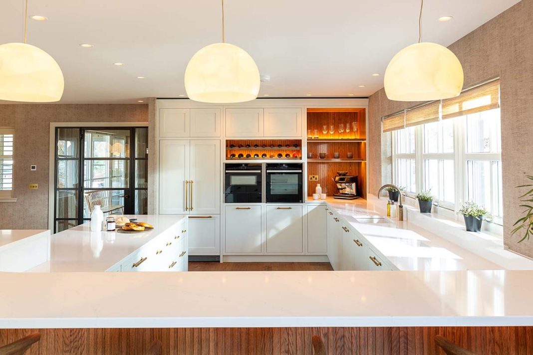 grand kitchen in traditional home in Scotland with hardwood paneling and floors as well as white cabinetry and subtle orange lighting for warmth