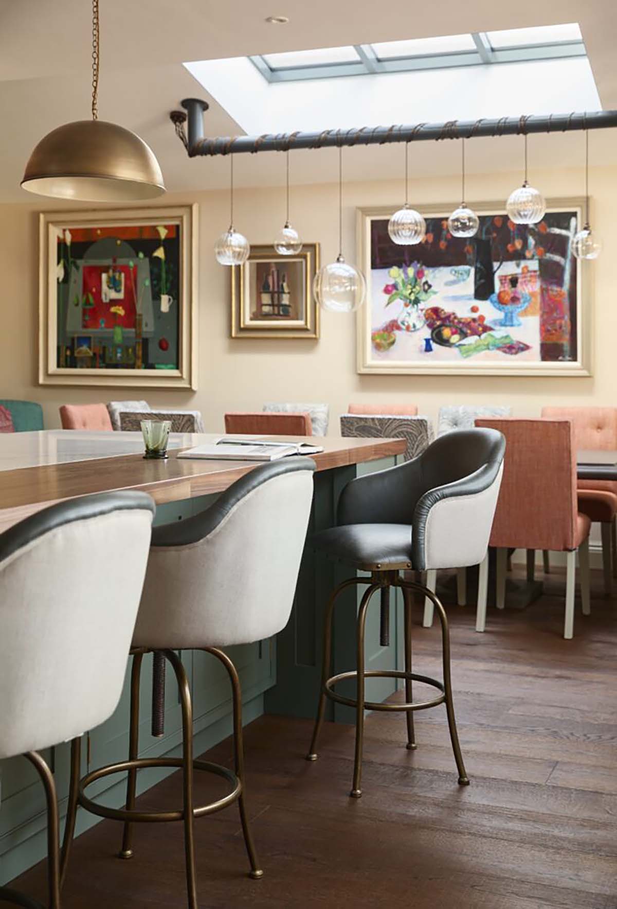 modern kitchen design with hard dark wood flooring, cream and green stools, copper pendant lights and art 