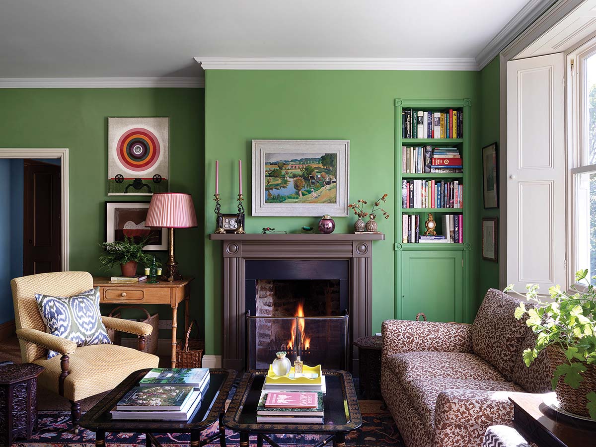 vibrant green living room with stone fire surrounds painted in black, offset by patterned sofas 