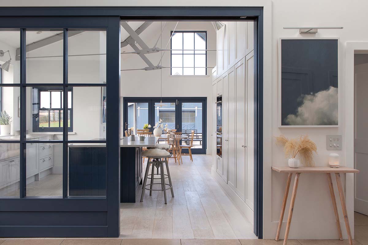 kitchen are leading into the dining room and living areas of honeyberry house in scotloand featuring blue walls, wood flooring and a triangular ceiling, enhanced by plenty of natural light. photography by dapple photography and design by architects at building workshop