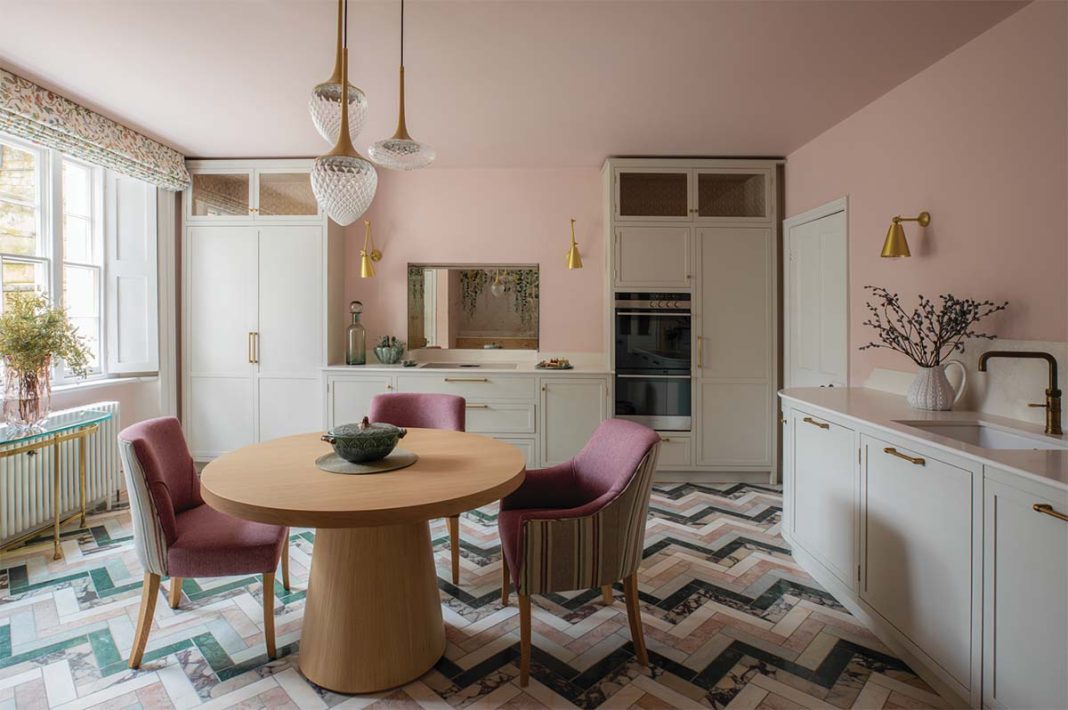 Pink kitchen with colourful herringbone flooring that accentuates the plants and golden fixtures of the room