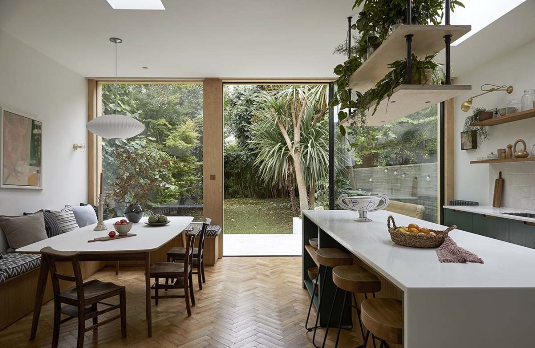 botanic house with indoor plants and patio doors that lead into a landscaped garden that focuses on an expansive lawn and exotic trees