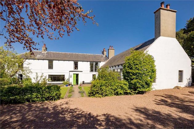 white cottage with a green door, stone driveway and green trees