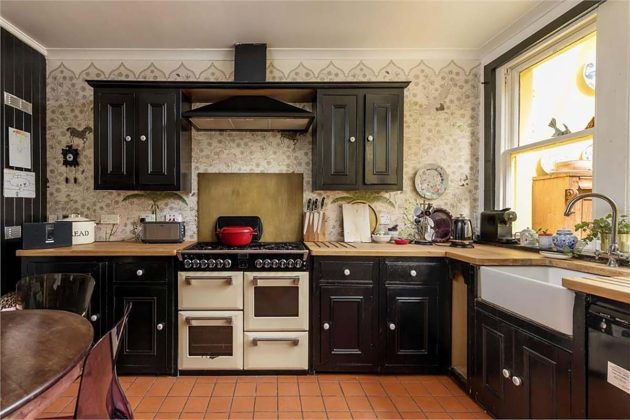 black and white traditional farmhouse kitche with white aga cooker, patterned wallpaper and black wooden cabinetry