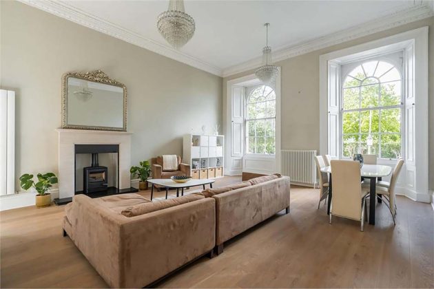 high-end homes for sale in Edinburgh; neutral boho living room scandi inspired style with black wood stove, brown sofas, brown carpets, round pendant lights and white radiators