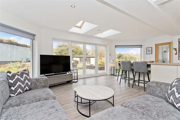 high-end homes for sale in Tanglewood; grey living toom with a white coffee table and grey bar stool seating at a breakfast bar with views of the garden