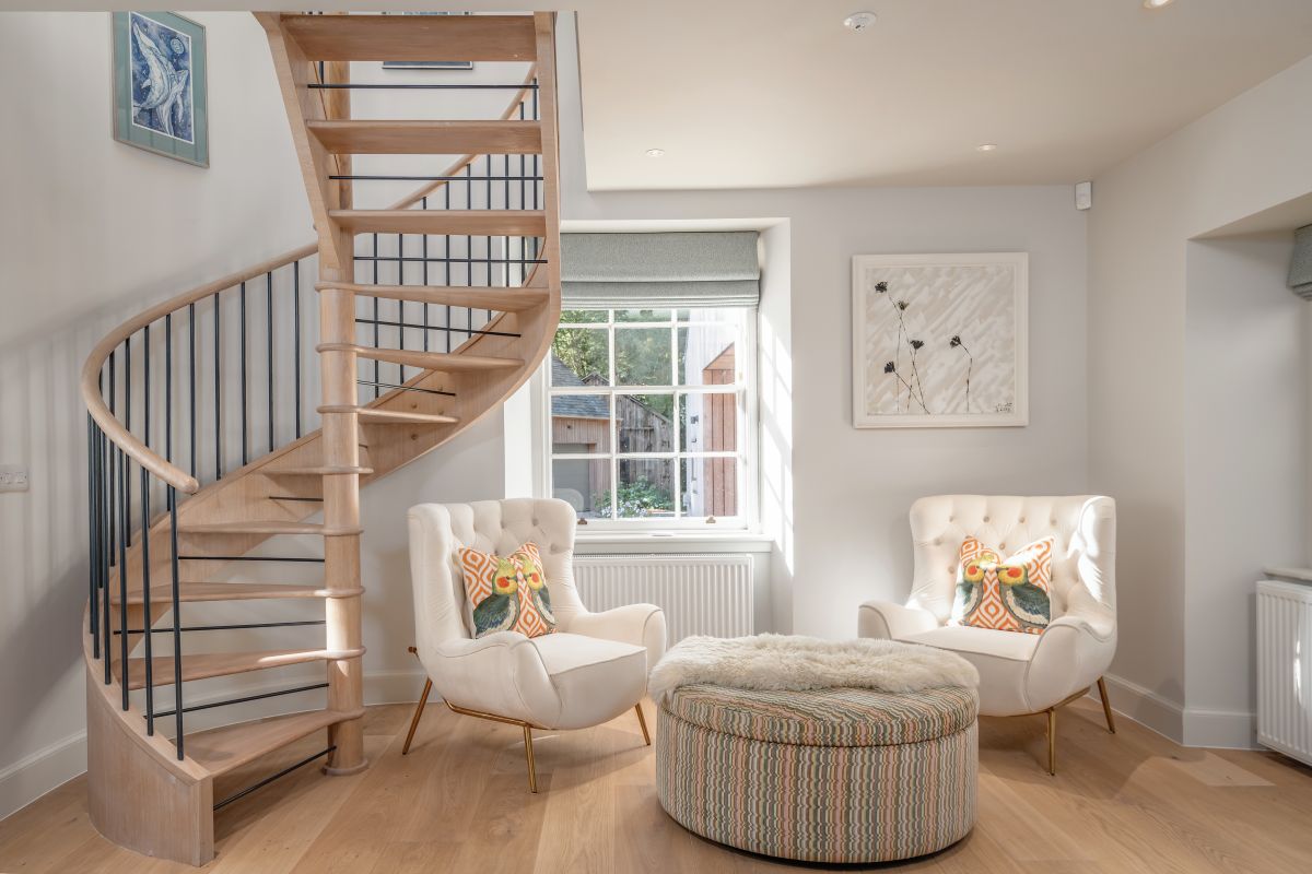 bright hallways with winding staircase in a victorian house with boucle white chairs window seat for reading