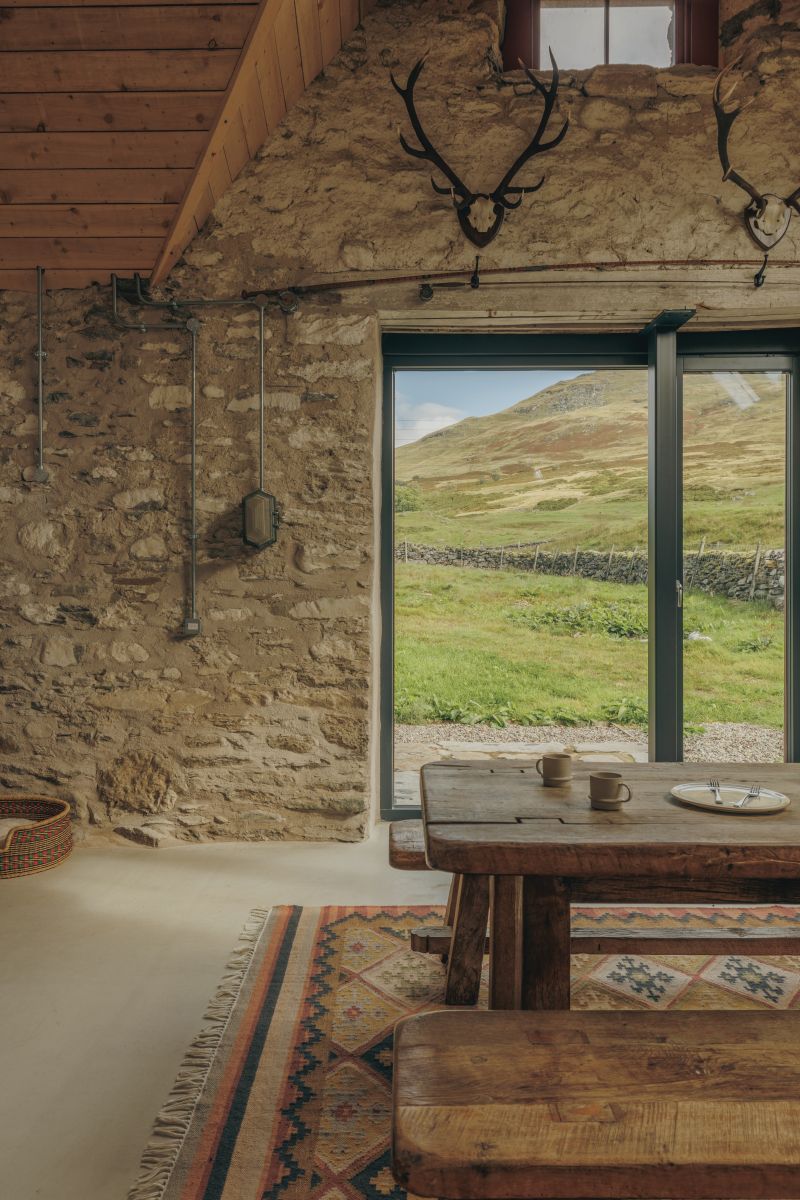 Modern elements such as the glazed door and exposed conduits sharply contrast with the old bare stone and natural timber