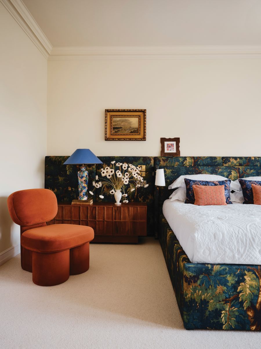 floral bed, orange headboard, orange armchair, velvet armchair, mid-century room, cream walls, blue lamp