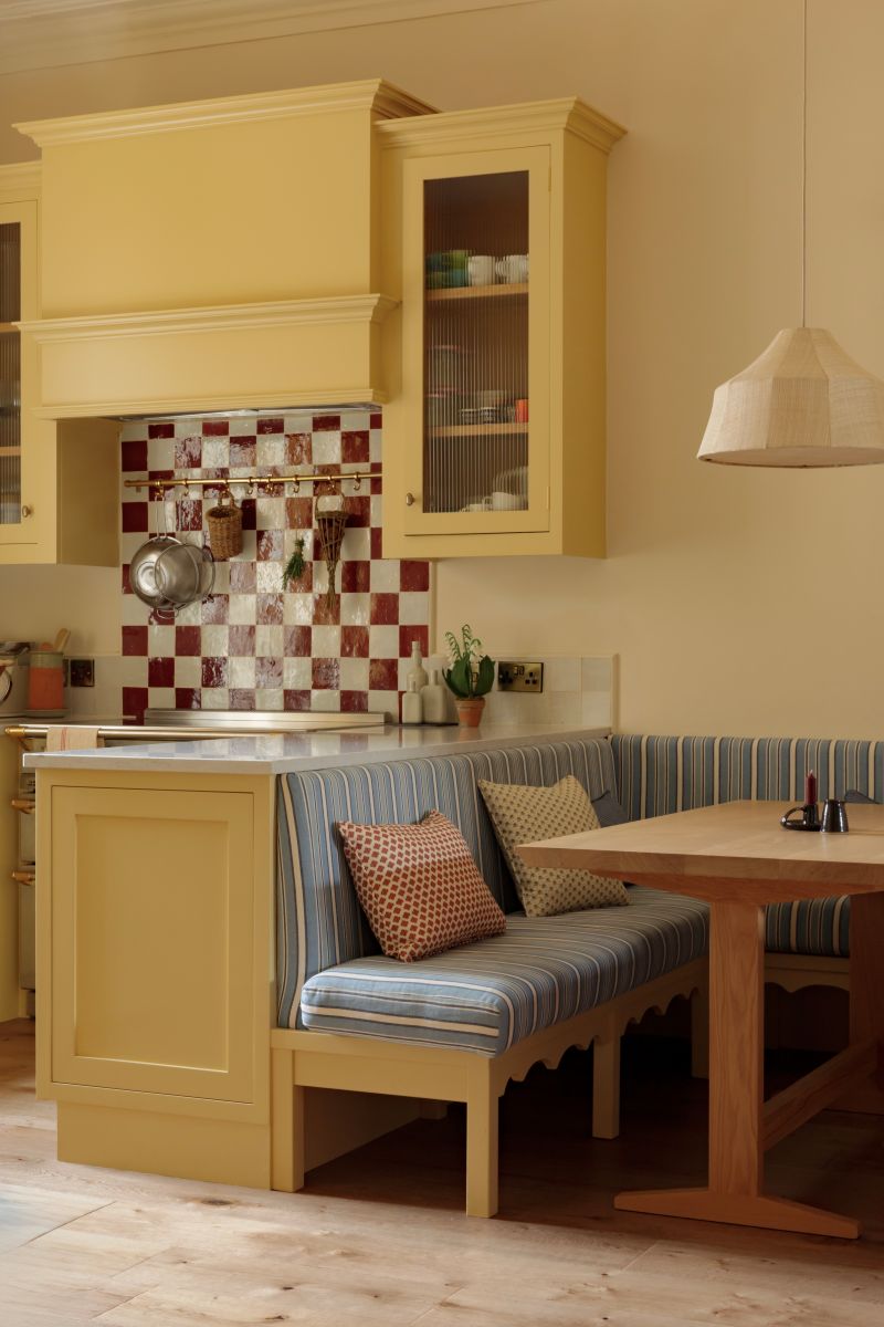yellow kitchen with dining table and tellow benches with blue cushions and red checkerboard splashback tiles