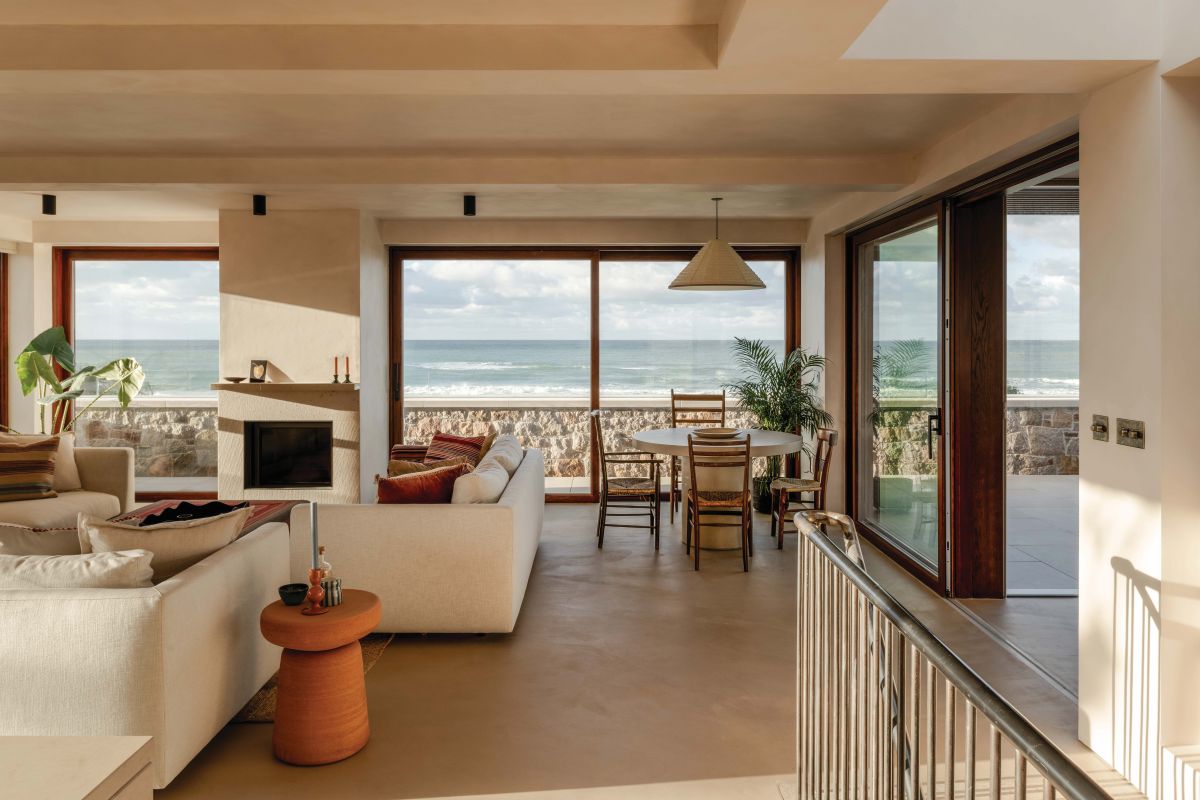sandy house by the beach with window walls and rattan lampshades and orange side tables
