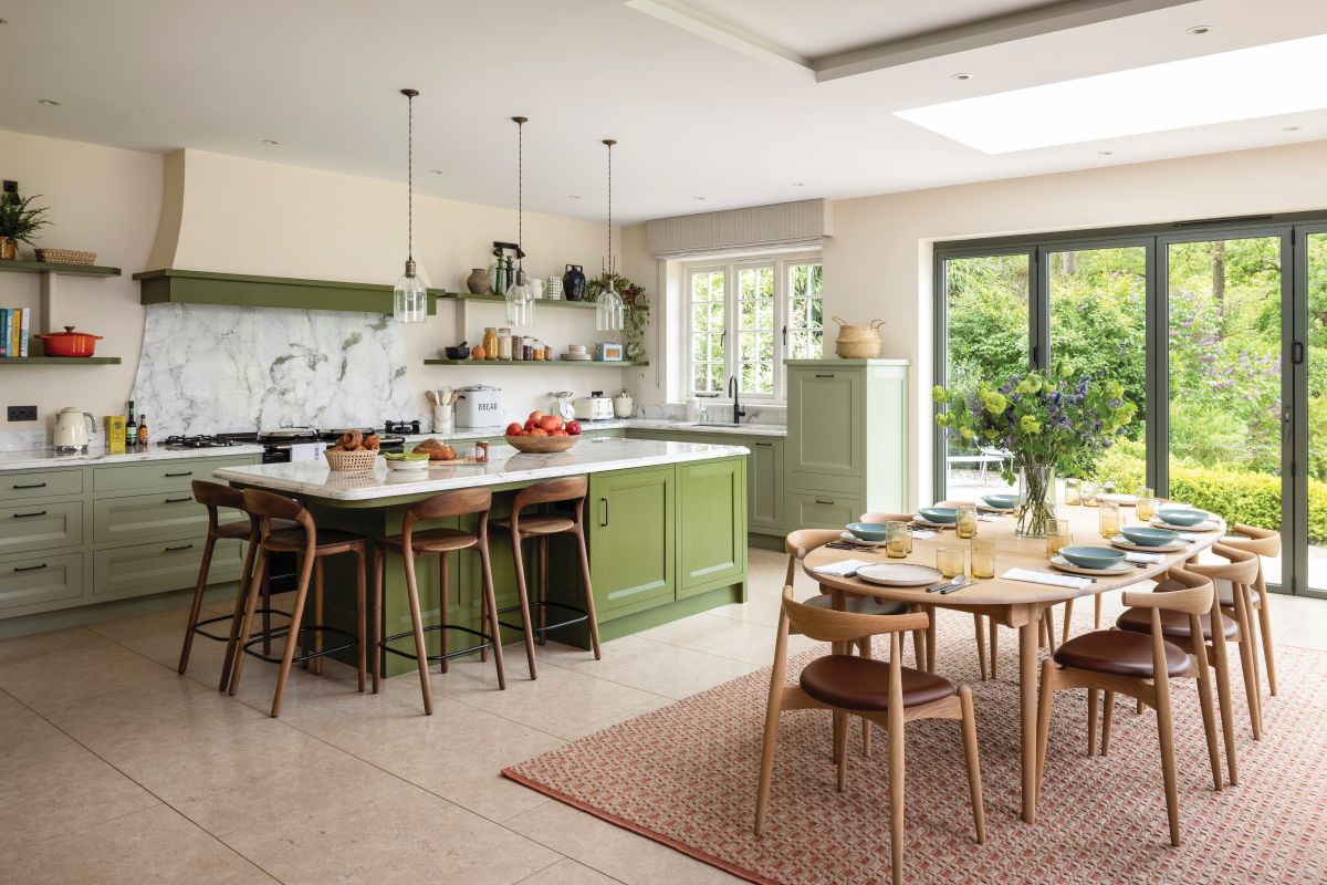 green cabinets in a kitchen and conservatory with rattan rug and oak dining table