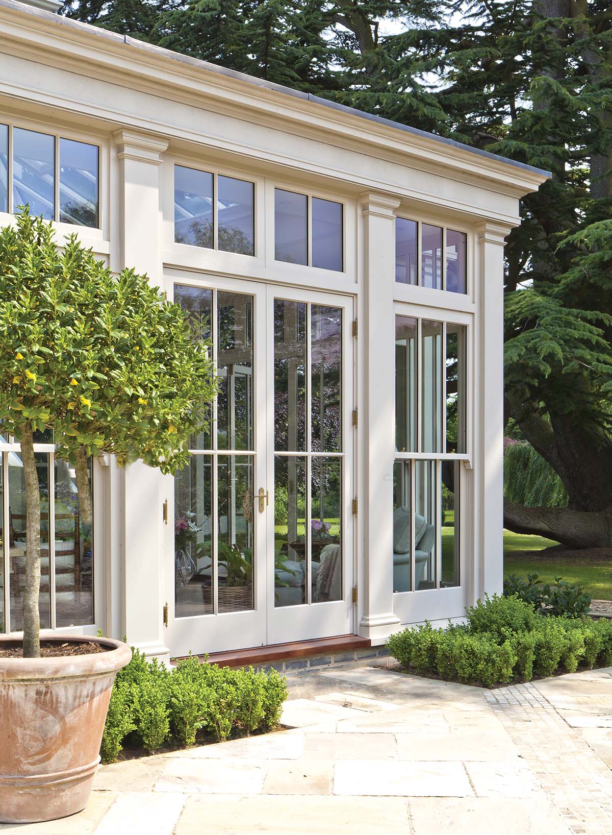 big white conservatory with big windows, a white patio and round tree